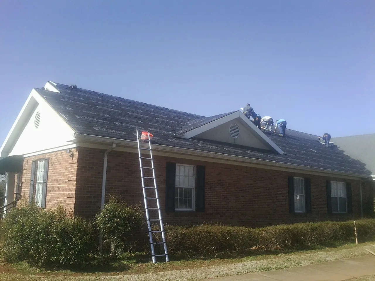 Crew tearing shingles off a brick ranch roof with a ladder set — Metal Roof Repair work by our crew in Fernwood