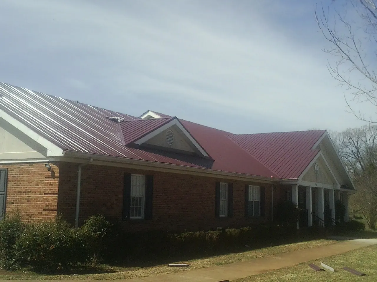 Red metal roof with gabled entries on a long brick building, from a Hail Damage Roof Repair job in Fernwood