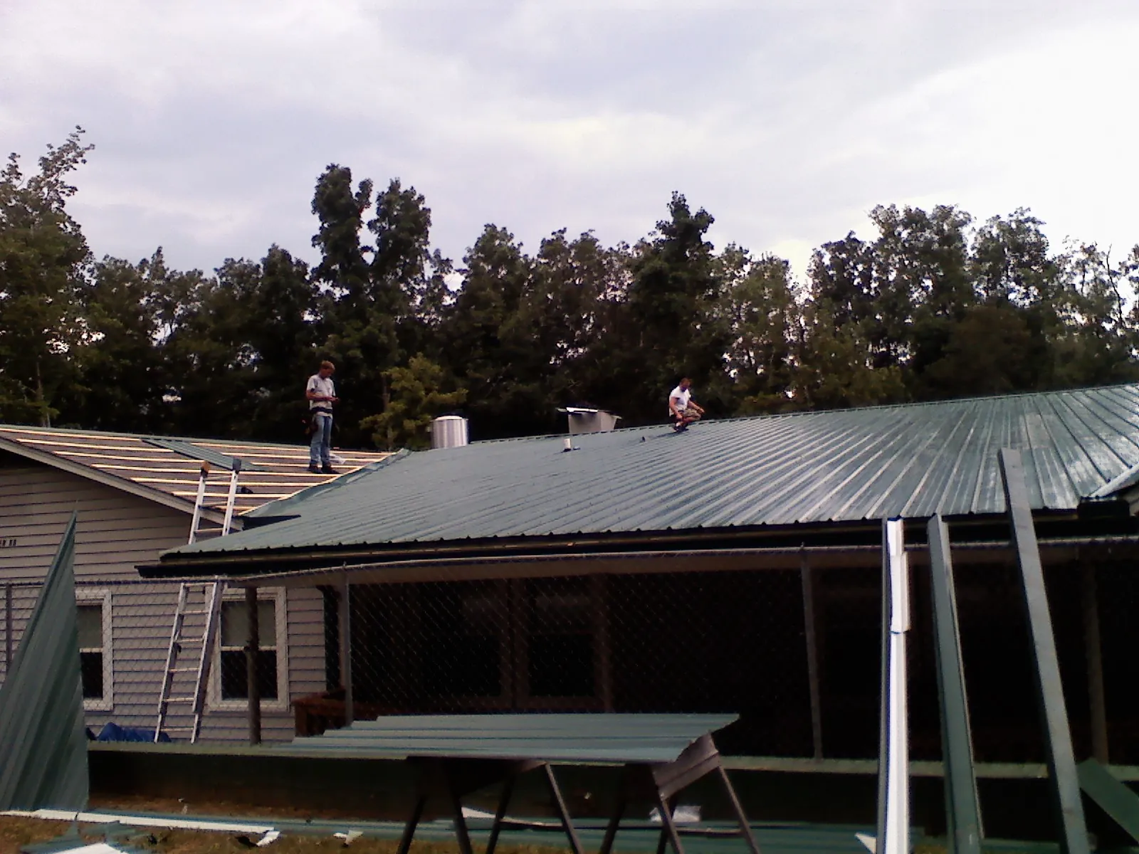 Two roofers installing green metal panels above a covered porch in Fernwood