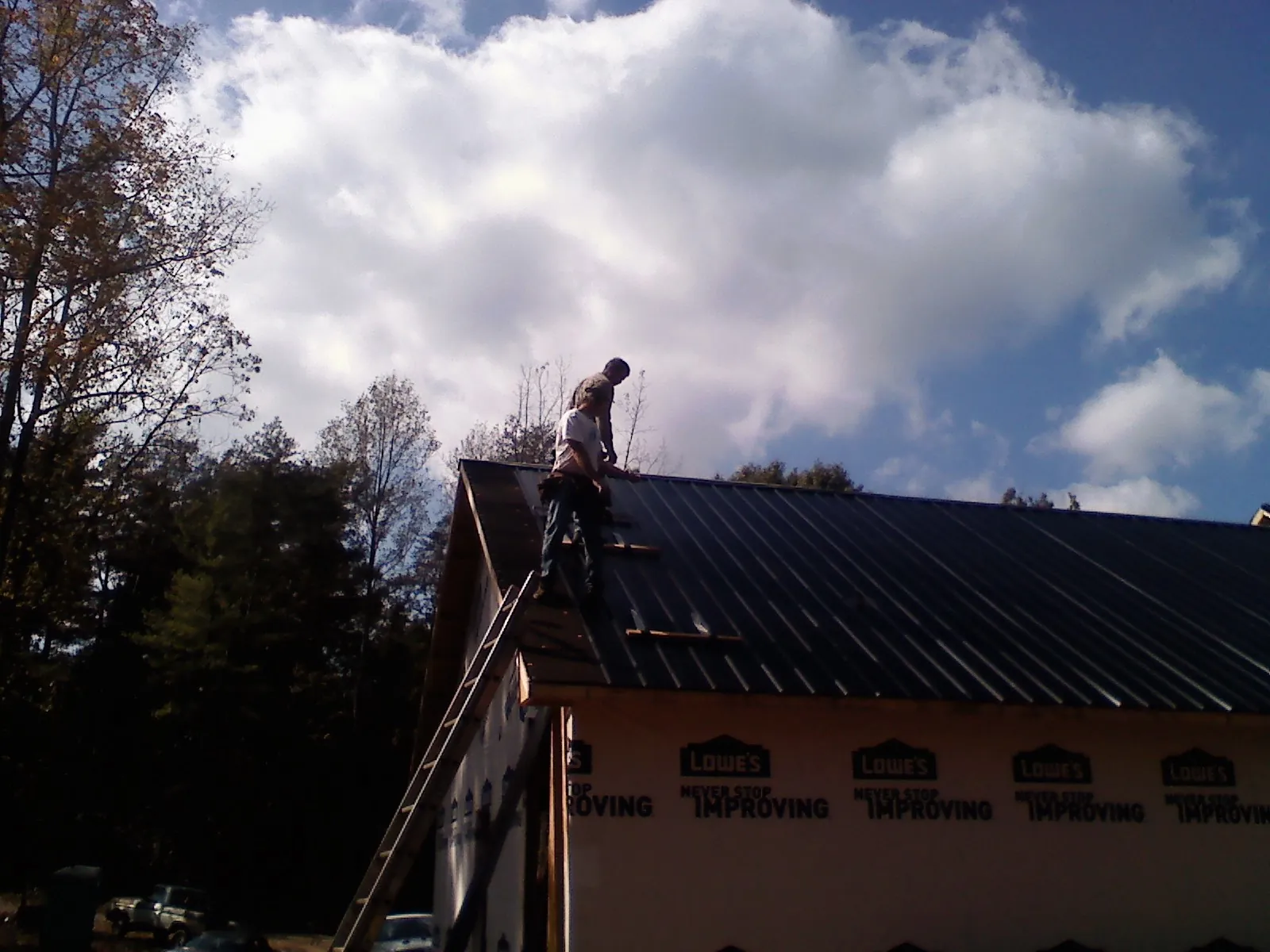 Roofer fastening dark metal panels high against a cloudy sky, from a Roof Inspection job in Fernwood