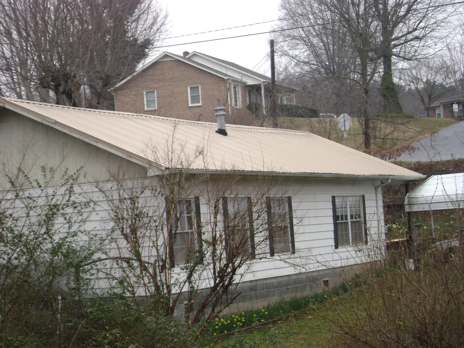 Tan metal roof on a white sided house set into a hillside — Commercial Roofing by Roofing Brothers in Fernwood